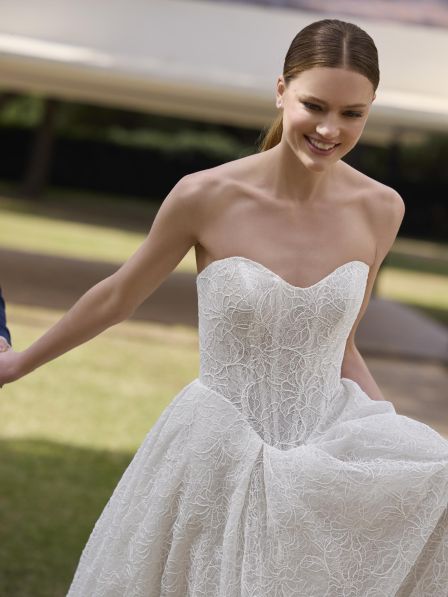 Woman in a white lace wedding dress standing outdoors.