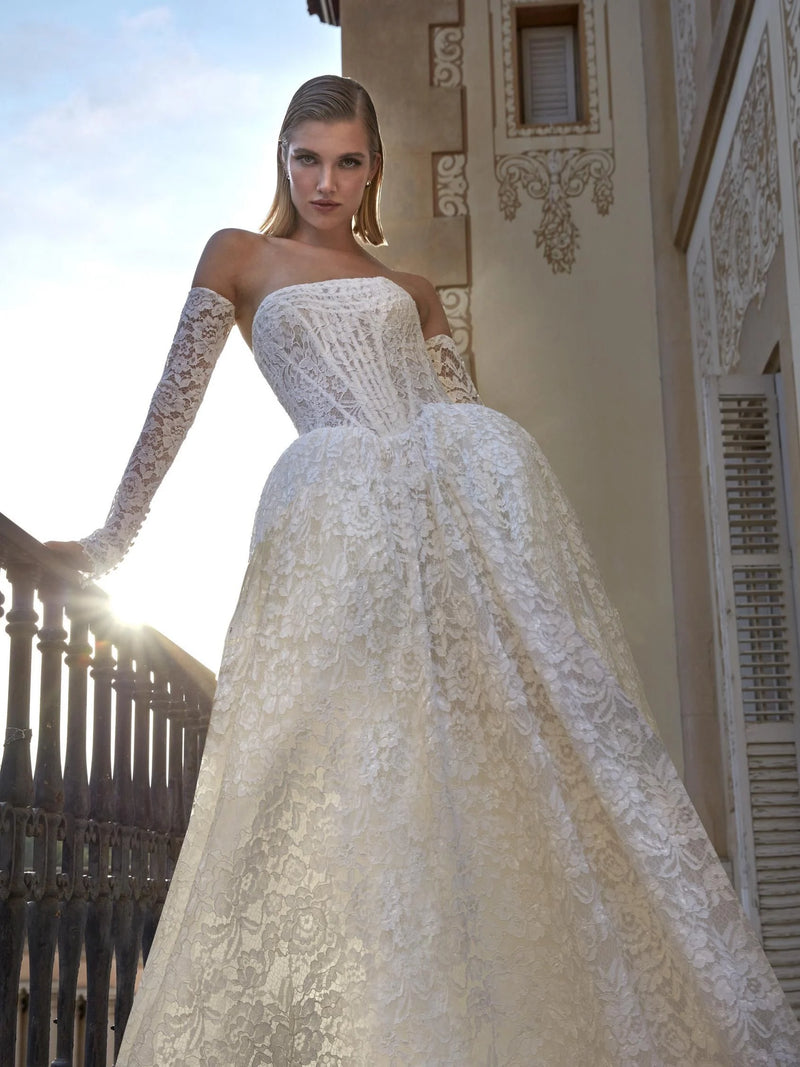 Woman in a white lace wedding dress standing on a balcony with sunlit background