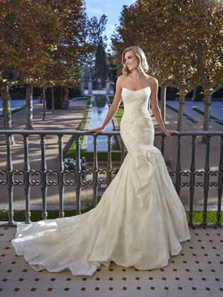 Woman in a white wedding dress by Pronovias BEEGOLD standing on a balcony with trees and water in the background