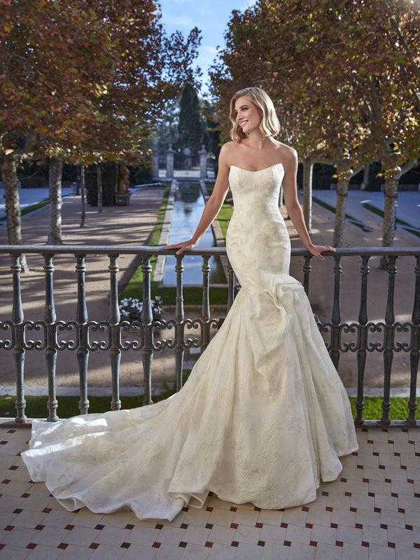 Woman in a white wedding dress by Pronovias BEEGOLD standing on a balcony with trees and water in the background