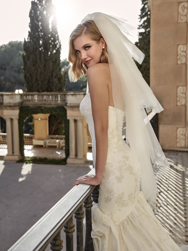 Bride in a white wedding dress with a long veil standing on a balcony.