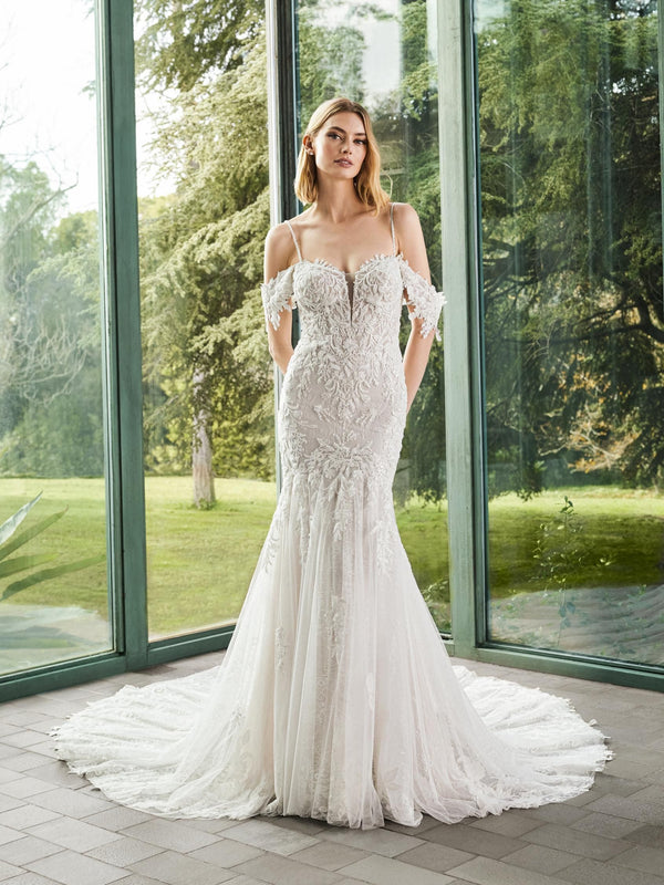 Woman in a white wedding dress by Pronovias ELIE standing in front of large windows with a green outdoor view.