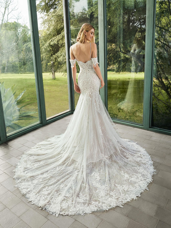 Woman in a white wedding dress by Pronovias ELIE standing in front of large windows with a green outdoor view.