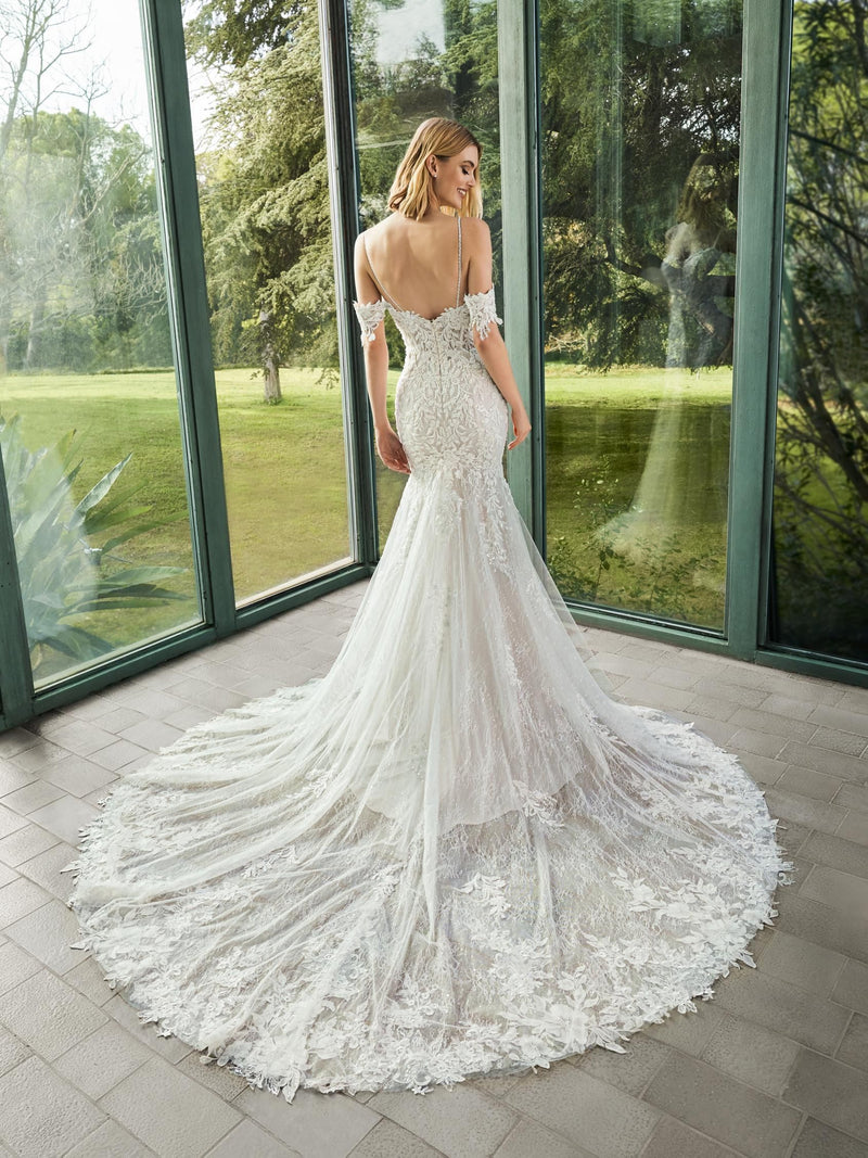 Woman in a white wedding dress by Pronovias ELIE standing in front of large windows with a green outdoor view.