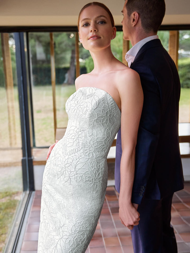 Woman in a strapless white lace wedding dress standing next to a man in a dark suit.