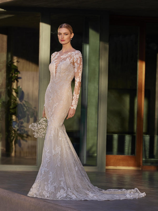 Woman in a lace wedding dress by Pronovias ILA standing in front of a modern building entrance.