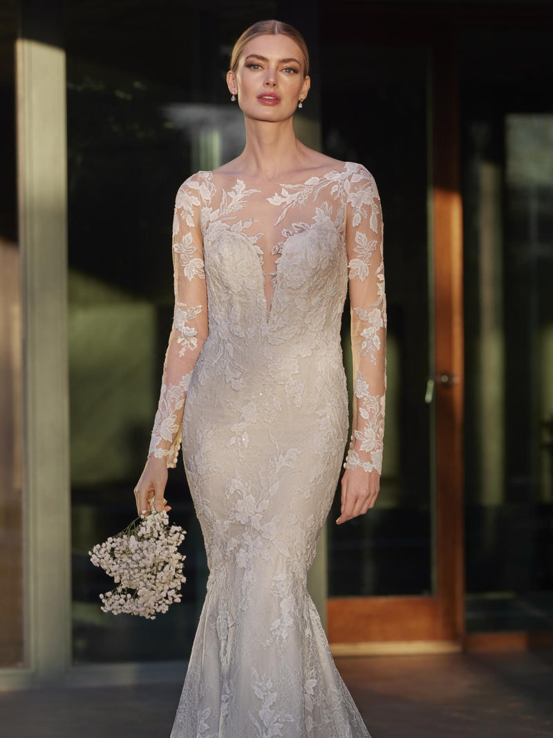 Woman in a lace wedding dress by Pronovias ILA holding flowers in an outdoor setting