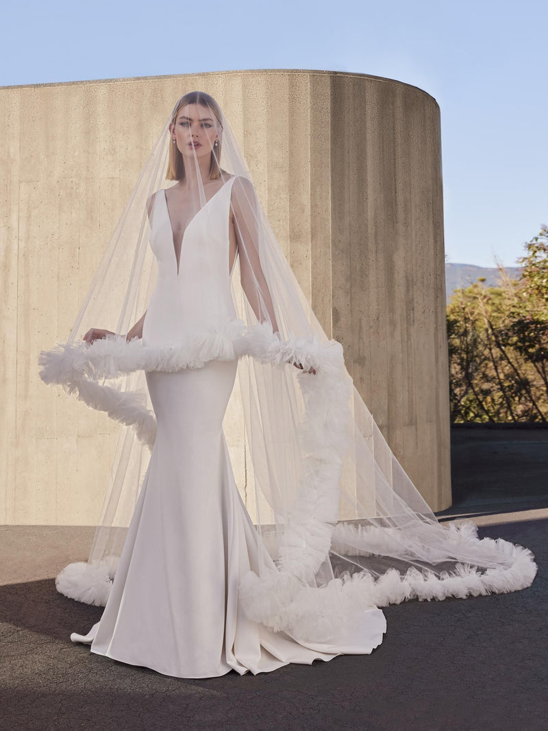 Woman in a white wedding dress with a long veil standing in front of a modern architectural structure ponovias snowbeet modern veil