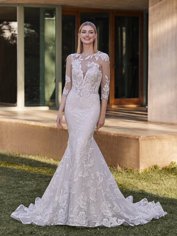 Woman in a white lace wedding dress by Pronovias YAI standing outdoors.