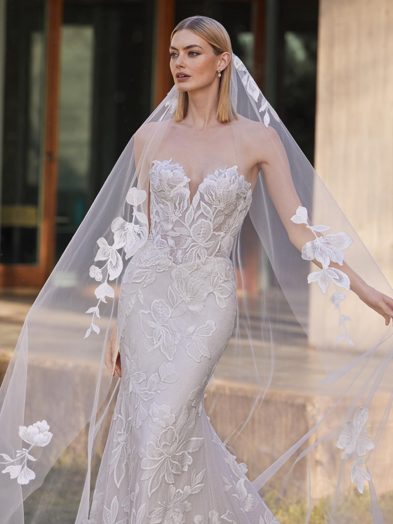 Woman wearing a strapless wedding dress with floral lace details and a long veil.